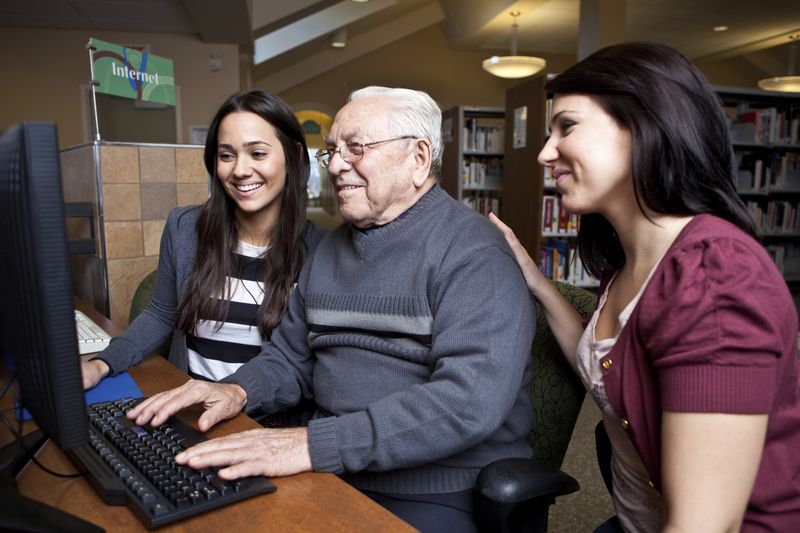 Volunteers teaching older man on computer
