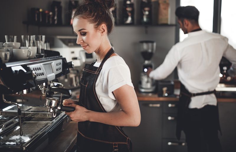 Young barista preparing coffee using a professional coffee machine in a coffee shop