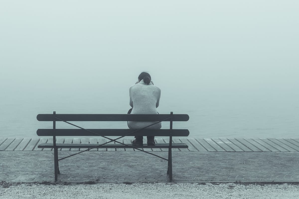 Person sitting on bench in front of foggy lake