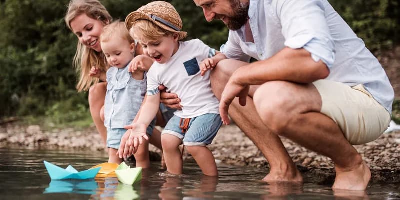 Young family with two toddler children outdoors by the river in summer, playing, by Halfpoint / Adoube Stock