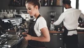 Young barista preparing coffee using a professional coffee machine in a coffee shop