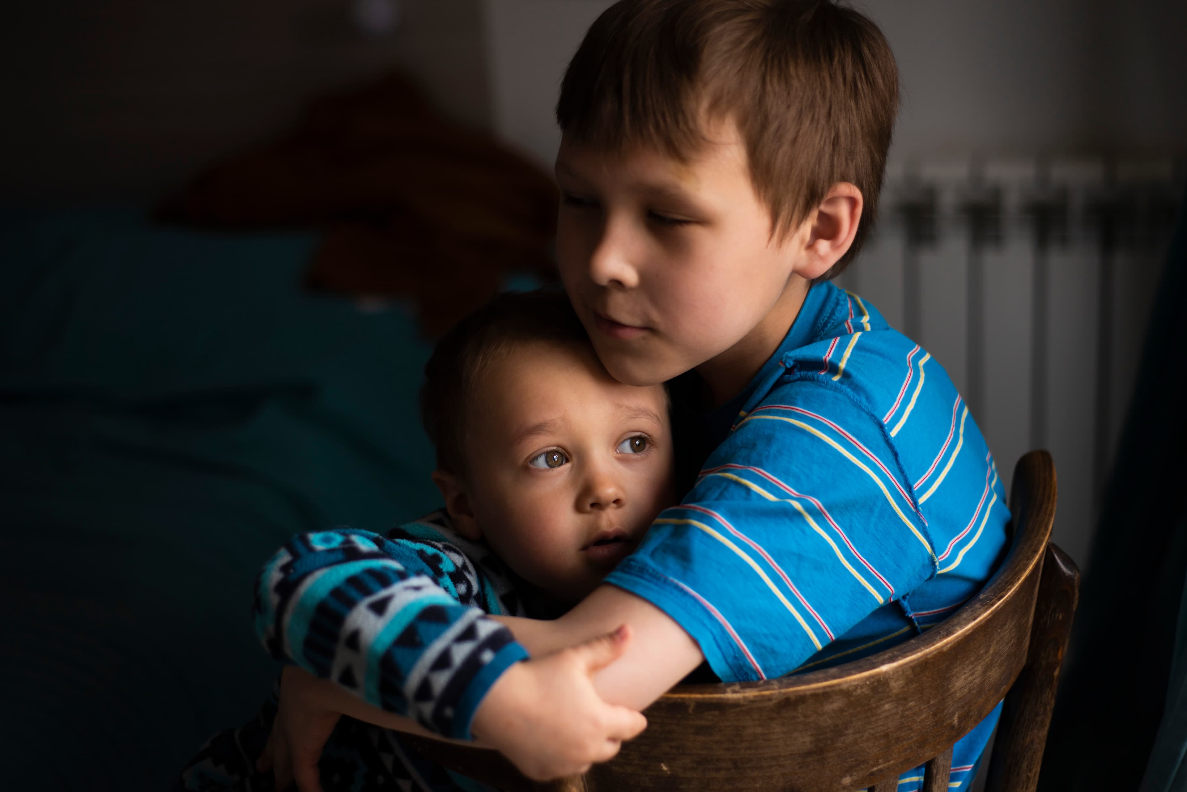 Young child holding toddler in their arms sitting on a chair