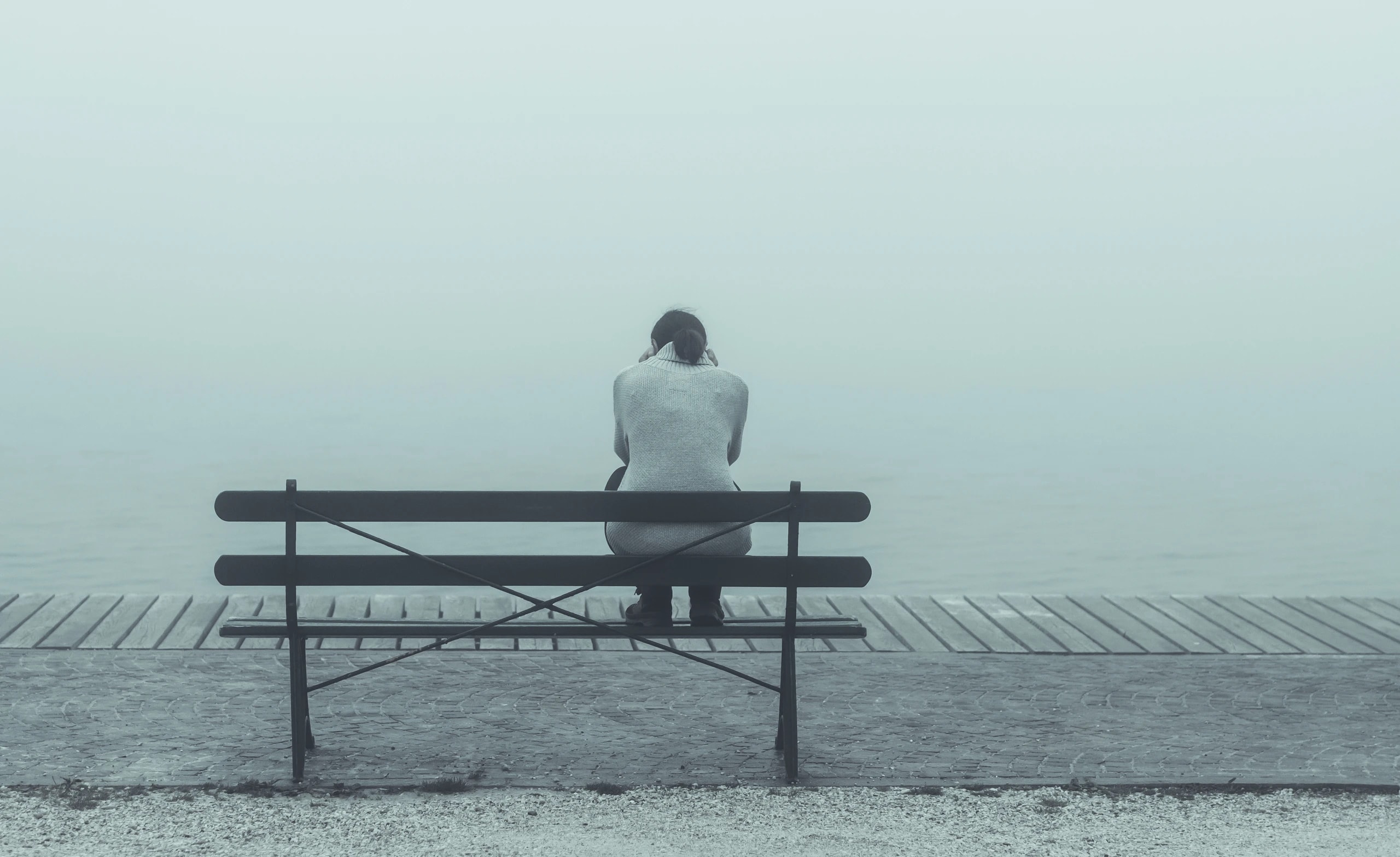 Person sitting on bench in front of foggy lake
